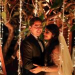 A romantic wedding reception scene with a smiling bride and a happy groom embracing under cascading white lights holding each other.