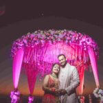 The new weds stands beneath a large, ornate floral archway.