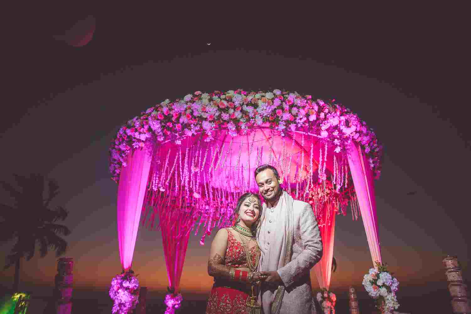 The new weds stands beneath a large, ornate floral archway.