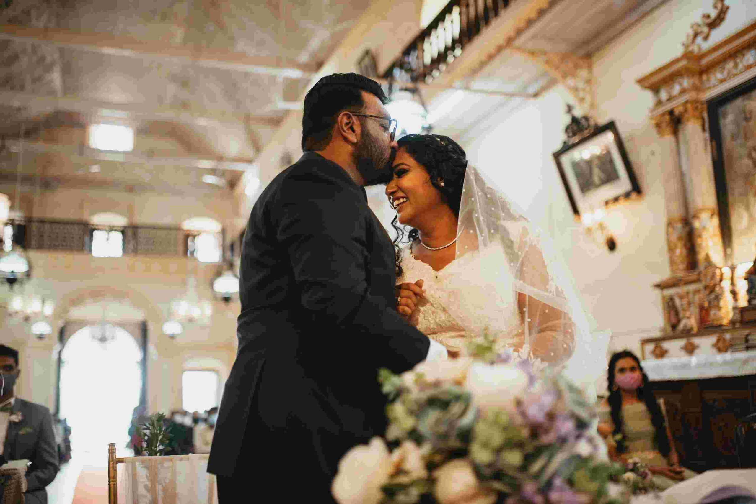 The bride smiles her heart out as her to be husband kisses on the forehead.