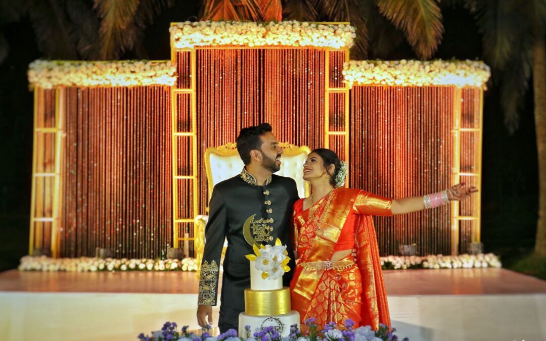 A couple smiling at each other while standing in front of a wedding cake.