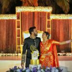 A couple smiling at each other while standing in front of a wedding cake.
