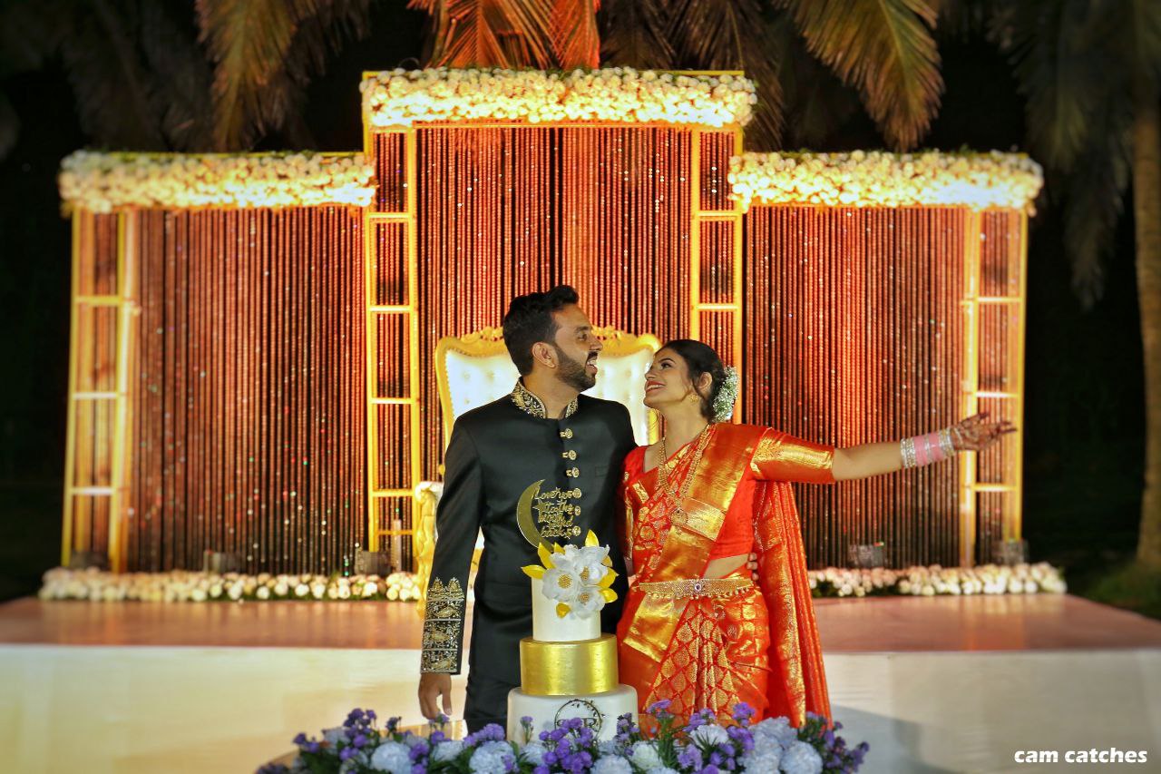 A couple smiling at each other while standing in front of a wedding cake.