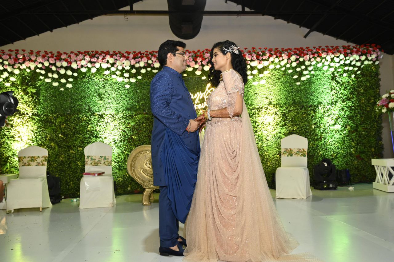 The couple smiling at each other while the elaborate floral decor behind a perfectly lit up