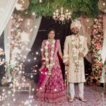 A newly married couple holding hands under a flower adorned archway.