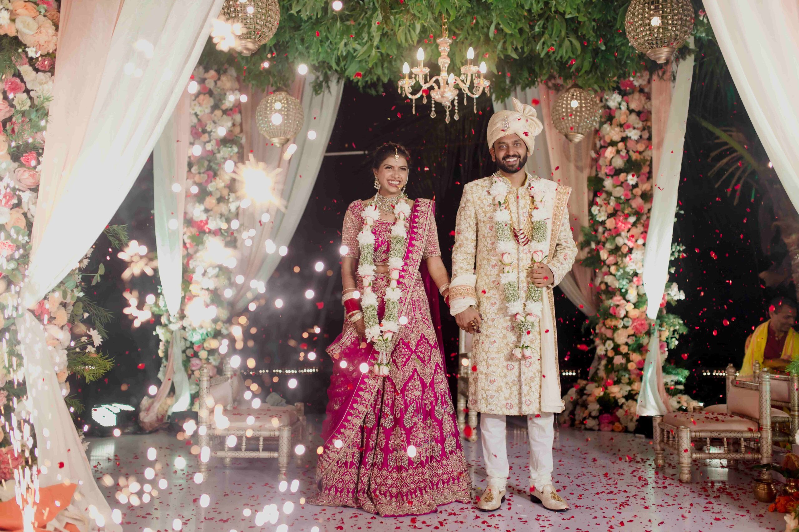 A newly married couple holding hands under a flower adorned archway.